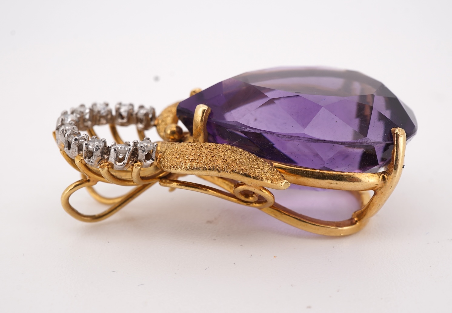 An Amethyst and diamond pendant, claw-set with a pear-shaped amethyst, topped with a foliate surmount in textured gold, accented with and arc of brilliant-cut diamonds totalling approximately 0.30 carats, length 3.5cm, s